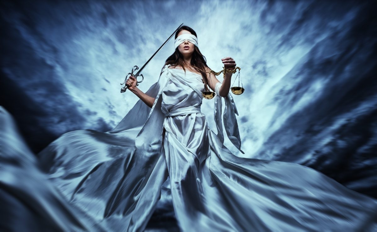 Femida, Goddess of Justice, with scales and sword wearing blindfold against dramatic stormy sky